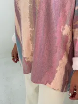 Sweater de punto con diseño abstracto en tonos rosados, beige y azul, de corte holgado, cuello en V y mangas largas con puños vueltos.