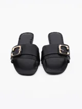 Sandalia tipo chinela color negro, con tira ancha sobre el empeine y aplique metálico dorado en forma de hebilla.