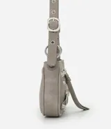 Cartera tipo baguette de PU color beige claro, con acabado liso y detalles de apliques metálicos tipo tachas y argollas en color gunmetal. Presenta un bolsillo frontal con cierre y un tirador de cuero sintético colgante. Incluye asa corta ajustable con hebilla.