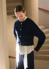 Chaqueta corta de denim color azul oscuro, con cuello redondo, cierre frontal de botones y dos bolsillos de parche delanteros.