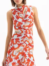 Vestido midi sin mangas con estampado floral en tonos rojos y celestes, cuello alto y detalle fruncido en el centro delantero.