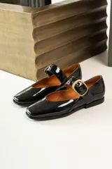 Zapato tipo Mary Jane de charol negro con hebilla dorada.