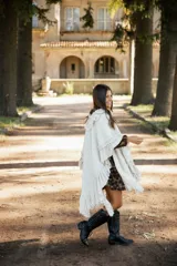 Ruana de lana merino color crudo, con diseño de silueta amplia y caída fluida. Presenta detalles de volados en lino a lo largo de la prenda y terminaciones con flecos en el ruedo.