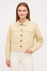 Sobrecamisa de denim en color gris lavado, con corte cropped, cuello clásico y cierre frontal mediante botones metálicos. Presenta costuras horizontales decorativas en el pecho y mangas largas con puños abotonados.