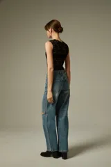 Pantalon de jean azul con corte recto y ancho, presenta aberturas en las rodillas y detalles de tachas metálicas a lo largo de las costuras laterales.