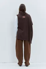 Poncho asimétrico de tejido de punto en color marrón, con cuello alto tipo polera y diseño sin mangas con aberturas laterales.