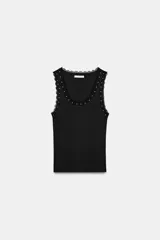 Musculosa de algodón color negro, con escote redondo y tiras anchas. Presenta detalles de encaje negro en los bordes y aplicación de perlas pequeñas alrededor del escote y los hombros.