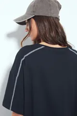 Remera de manga corta con silueta relajada y costuras a la vista en color blanco que contrastan sobre el tejido negro. Presenta un diseño moderno con terminaciones destacadas.