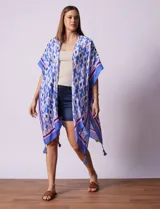 Kimono tejido con estampado abstracto en tonos azules, blancos y violetas. Tiene terminación de ruedo con borlas.