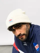 Gorro tipo beanie de tejido de punto color blanco crema, con parche frontal que incluye el logo de Umbro y la inscripción Nacional.