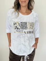 Remera blanca de la línea italiana con estampado frontal que combina bloques de animal print (leopardo y cebra) en tonos dorados y negros, y la frase "Find your true NATURE". Presenta un cuello redondo, mangas largas y un cordón regulable en la parte inferior para ajustar el largo.