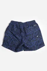 Short de baño celeste con estampado de hojas pequeñas en tonos verdes y blancos. Cuenta con cintura elástica con cordón ajustable, bolsillos laterales y un parche circular con logo en la parte inferior.