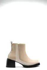 Bota corta de cuero en tono beige, con diseño bicolor que presenta un panel lateral en un tono más claro. Cuenta con un taco cuadrado negro de altura media y cierre lateral interno.