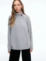 Sweater de tejido de punto en color gris, con cuello alto y cierre metálico lateral. Presenta un diseño de líneas verticales y corte holgado.