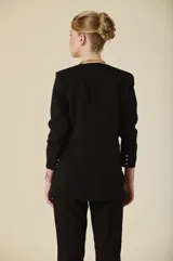 Saco de mujer color crema con diseño estructurado, cierre frontal de un botón dorado y bolsillos laterales con solapa. Presenta mangas tres cuartos con detalle de botones dorados en los puños.
