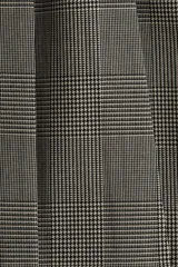 Pollera corta con pliegues marcados (tableada) y silueta evasé. Presenta un estampado de pata de gallo o príncipe de Gales en tonos grises y blancos.