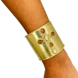 Brazalete dorado con forma de cruz adornada con piedras naturales.
