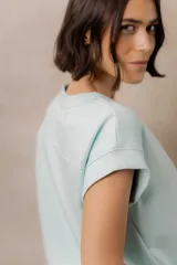 Sweater de punto color blanco, de corte relajado, con cuello redondo, manga corta japonesa de hombro caído y pretina ancha en la cintura.