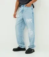 Pantalón de jean corte baggy, color celeste claro con efecto desgastado y estampado de lettering estilo grafiti en color blanco. Presenta cintura con trabillas, cierre frontal con botón y cremallera, y bolsillos laterales y traseros.