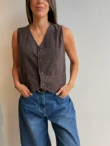 Chaleco de pana fina color marrón oscuro, con escote en V, cierre frontal de botones y corte entallado.