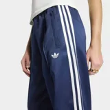 Pantalón deportivo Adidas SST de satén color azul marino, de corte holgado y diseño de pernera ancha. Cuenta con las clásicas tres tiras blancas a lo largo de los laterales y el logo del trifolio bordado en una pierna.