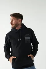 Buzo canguro negro con capucha ajustable y bolsillo frontal. Presenta un estampado gráfico en el pecho con texto y líneas decorativas, además de un detalle estampado en la manga.