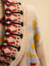 Cardigan de tejido grueso con cuello shawl, estampado tribal en tonos crema, rojo arcilla y negro, con cierre frontal de botones.