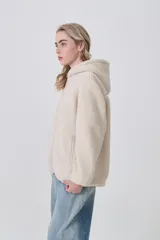 Campera de corderito con capucha, cierre frontal completo y bolsillos laterales. Presenta un diseño holgado de manga larga en color beige.