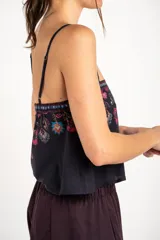Top corto negro con tirantes finos, escote recto y diseño holgado. Presenta un estampado estilo paisley con detalles en tonos fucsia, turquesa y verde, además de una cenefa geométrica en la parte superior.