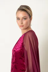 Vestido largo de fiesta color granate, confeccionado en terciopelo con cuello redondo adornado con strass y capa de chifón que nace de los hombros.