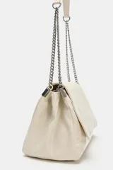 Bolso de hombro color crudo con solapa frontal y diseño estructurado con costuras decorativas. Cuenta con correa mixta de cuero y cadena metálica plateada.