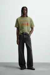 Camiseta de punto de algodón con corte relaxed fit, cuello redondo y manga corta. Color verde oliva con efecto lavado y estampado frontal con diseño gráfico en tonos rojo y amarillo.