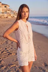 Blusa de algodón sin mangas en color blanco off-white, con cuello alto con volados y cierre frontal de cordones ajustables con lazos. Presenta detalles de encaje y bordados sutiles en la parte delantera.