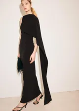 Vestido largo negro de corte entallado y diseño asimétrico, sin mangas, con detalle de capa en el cuello y fruncidos laterales.