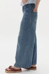 Pantalón de jean de pierna ancha y tiro alto, con bolsillos delanteros y traseros, presillas para cinturón y costuras verticales al frente.