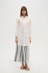 Camisa blanca de manga larga, corte holgado y largo, con cuello camisero y botones frontales. Presenta bordados florales en tono blanco sobre el tejido.