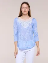 Blusa celeste con estampado floral devoré, de manga tres cuartos, escote redondo amplio y detalle de pechera de encaje blanco en contraste.