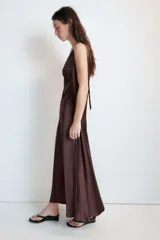 Vestido midi satinado color marrón, con escote en V y tirantes anchos ajustables con lazada en los hombros. Presenta cierre lateral con cremallera oculta.