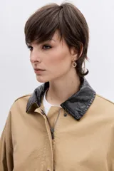 Cazadora de corte oversize en color beige, con cuello de solapa en contraste de color oscuro, cierre frontal con botones y bolsillos laterales.