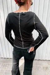 Remera de manga larga color negro, con cuello redondo y diseño de costuras verticales expuestas en color blanco que recorren el frente y las mangas.
