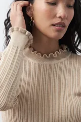 Polera de tejido acanalado con cuello y puños con volados. Presenta una silueta entallada y textura vertical que estiliza la figura.