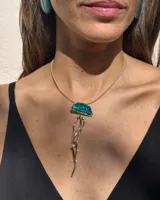 Collar de cadena fina dorada con un dije artesanal en forma de medusa, elaborado en bronce con detalles en resina de color turquesa.