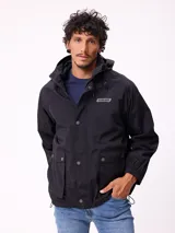 Campera impermeable Rusty con capucha, confeccionada en nylon. Presenta cierre frontal con botones a presión, bolsillos delanteros con solapa y puños elásticos.