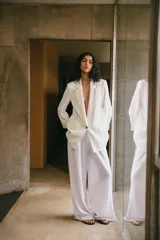 Blazer blanco de lino con cuello solapa, manga larga con hombreras y puños con vuelta estampada. Tiene bolsillos delanteros con solapa y cierre frontal con botón.