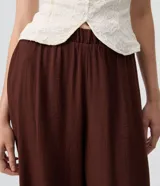 Pantalón bloomer marrón de cintura alta, confeccionado en viscosa con textura crinkle. Cuenta con un diseño amplio y cómodo, perneras voluminosas, puños con elástico interno y aplicación de encaje floral en los puños.
