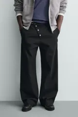 Pantalón wide fit de algodón con efecto lavado, corte recto y holgado. Presenta un cierre frontal cruzado con botones y un alamar metálico distintivo, además de bolsillos frontales y traseros de plastrón.