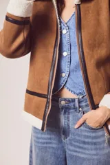 Campera marrón de gamuza sintética con cuello, puños y ruedo de piel sintética blanca. Presenta cierre frontal con cremallera, bolsillos laterales y detalles en cuero sintético negro.