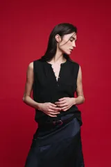 Blusa sin mangas color negro, de silueta fluida, con cuello redondo, detalle de alforzas en el frente y abotonadura parcial con botones visibles.