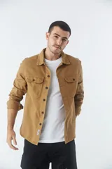 Sobrecamisa de jean color tostado, con cuello clásico, cierre frontal con botones y dos bolsillos frontales con solapa. Presenta mangas largas con puños abotonados y un pequeño parche decorativo en el ruedo.