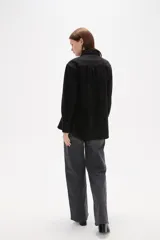 Camisa de jean negro con diseño de frunces verticales en el frente, cuello clásico, cierre frontal con botones y mangas largas con puños abotonados.